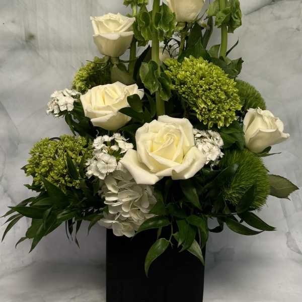 White roses and green blooms arranged in a black square vase