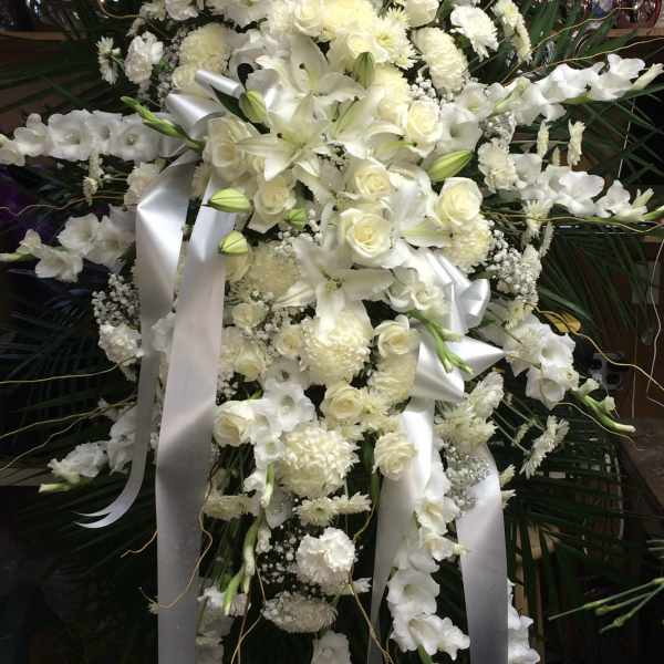 Large white funeral spray with lilies, roses, and ribbons