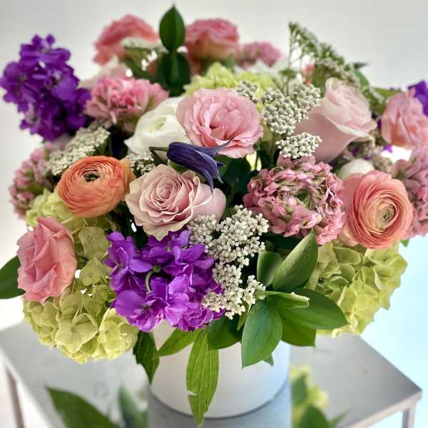 Mixed pink, purple, and green flowers arranged in a white box