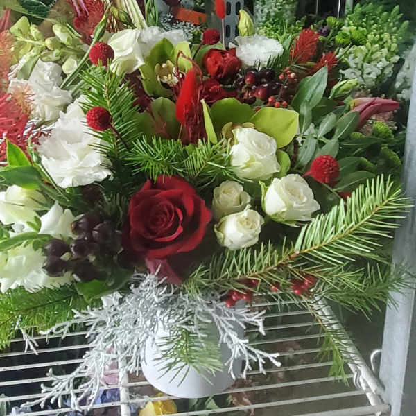 Red and white floral arrangement in a white container with pine accents