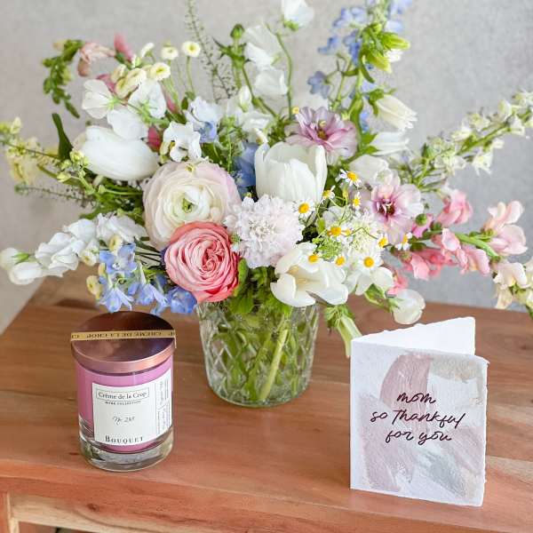 Mixed pastel bouquet in a clear glass vase beside a candle and thank-you card