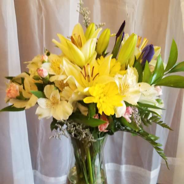 Yellow and white lilies with mixed flowers in a glass vase