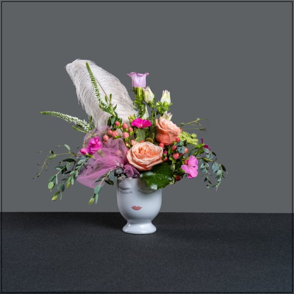 Pink and peach floral arrangement in a white face vase with a feather accent