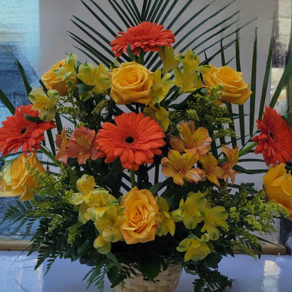 Basket arrangement of orange gerberas, yellow roses, and yellow orchids