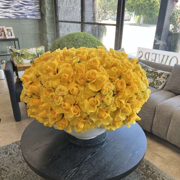 Large yellow rose arrangement in a white bowl vase on a round table