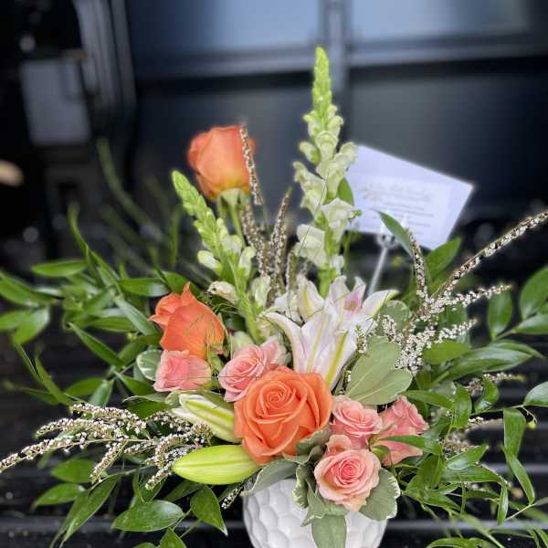 Coral and pink roses with white lilies in a white vase