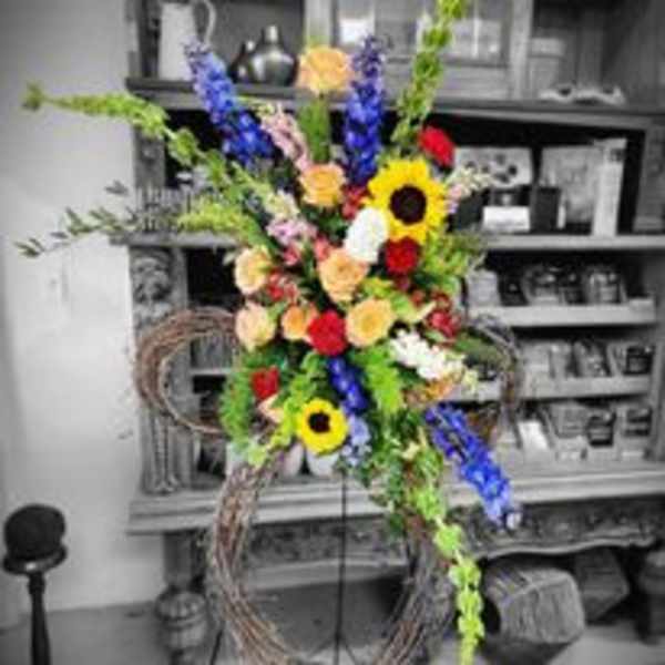 Tall floral standing spray with sunflowers, roses, and blue flowers