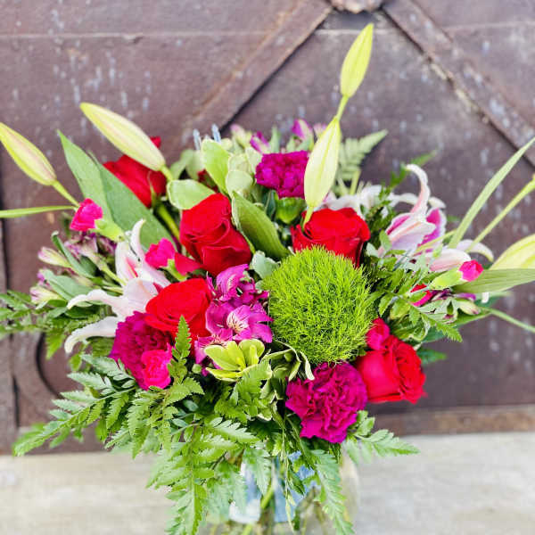 Mixed bouquet of red roses, pink blooms, and white lilies in a glass vase