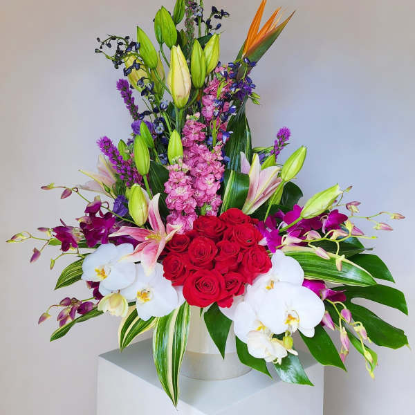 Mixed bouquet with red roses, white orchids, pink lilies, and purple flowers in a white vase