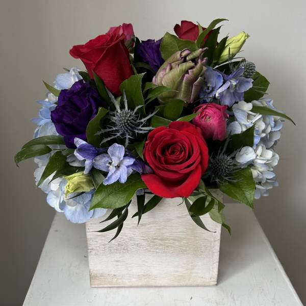 Mixed bouquet of roses, hydrangeas, and purple blooms in a white wooden box