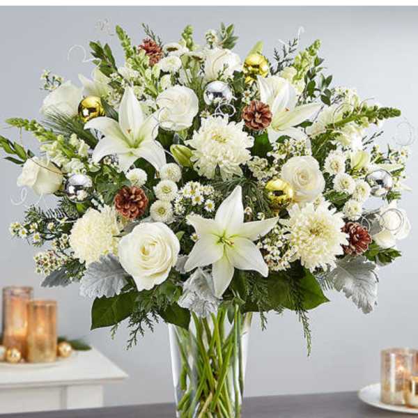 White lilies and roses in a clear glass vase with pinecones and ornaments