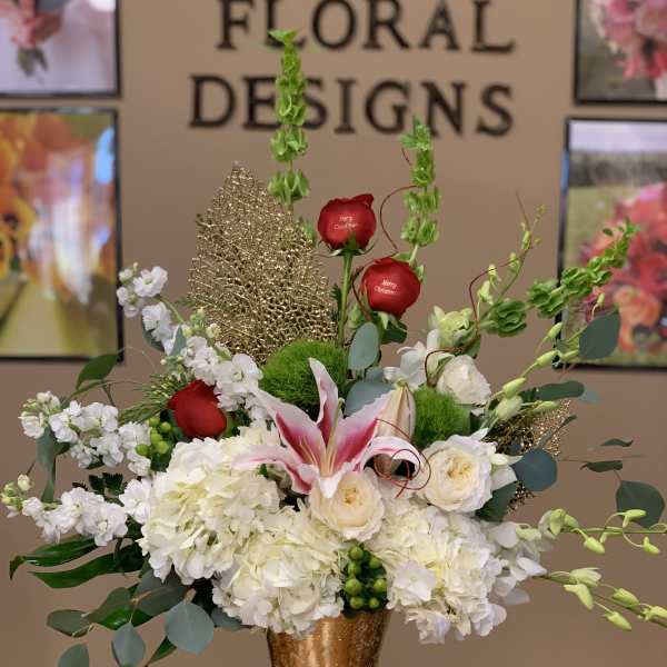 Tall floral arrangement with white blooms, red roses, and pink lilies in a gold vase