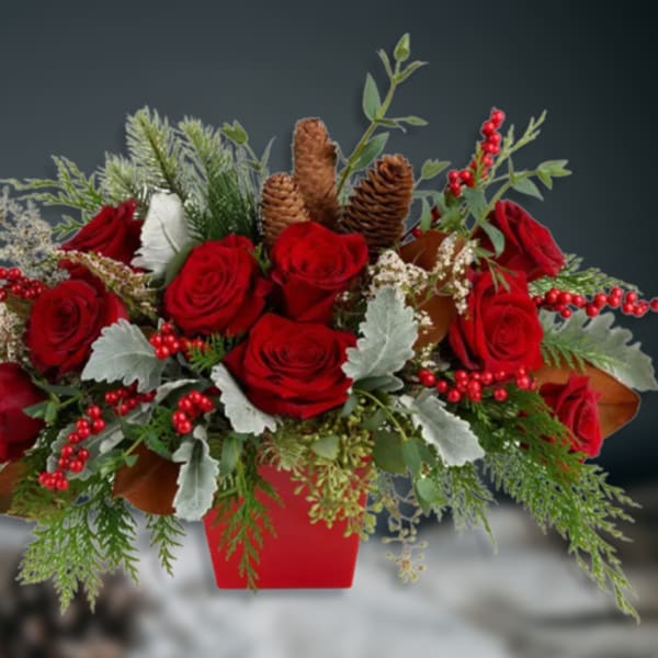 Red roses arranged in a red container with pinecones and berries