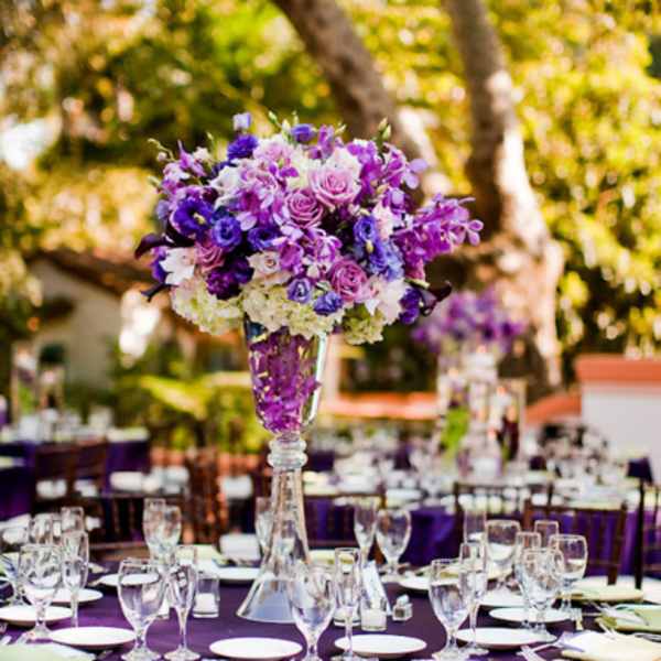 Purple floral centerpiece in a tall glass vase on a banquet table