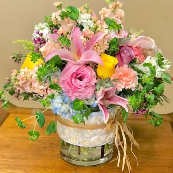Mixed bouquet of pink, peach, yellow, and blue flowers in a glass vase