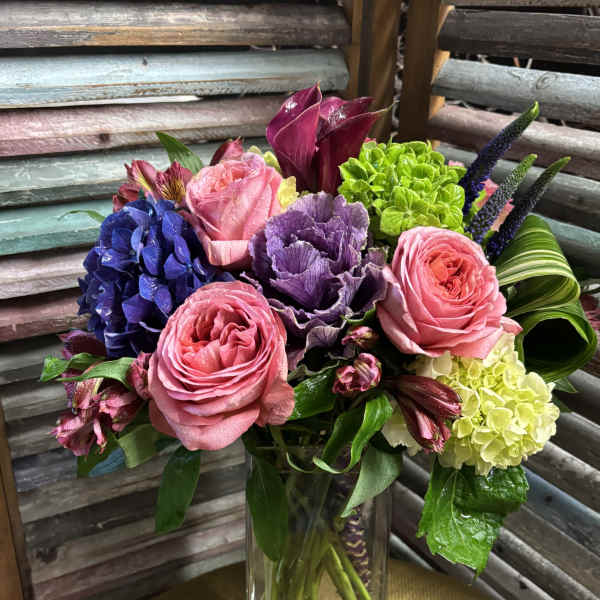 Mixed bouquet of pink roses, purple blooms, and green hydrangea in a glass vase