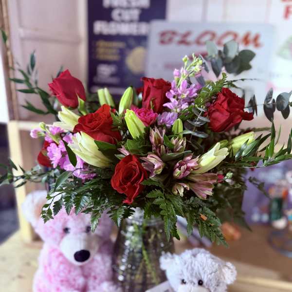 Bouquet of red roses and pink flowers in a glass vase with teddy bears