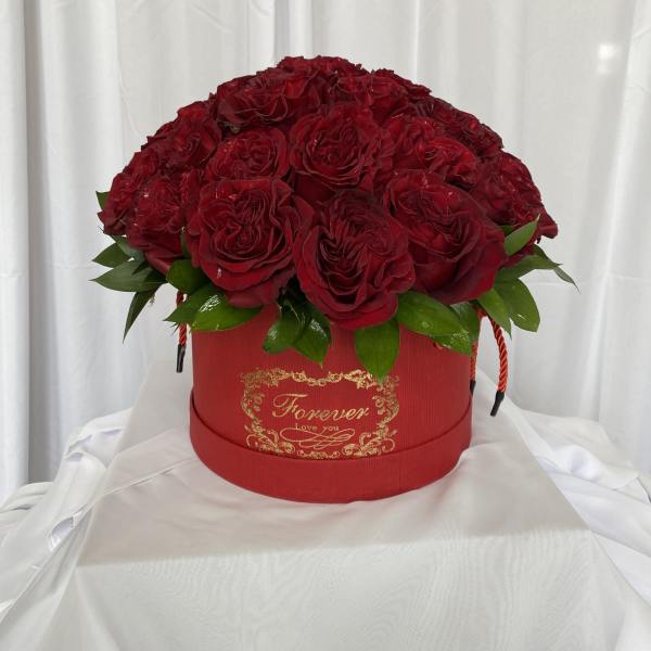Red rose arrangement in a round red box with gold lettering