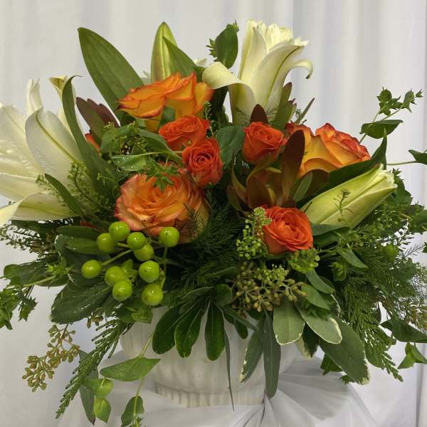 Orange and white roses arranged in a white vase with greenery