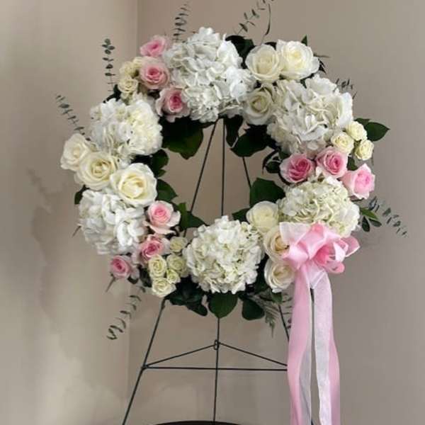 White and pink floral wreath on a stand with a pink ribbon