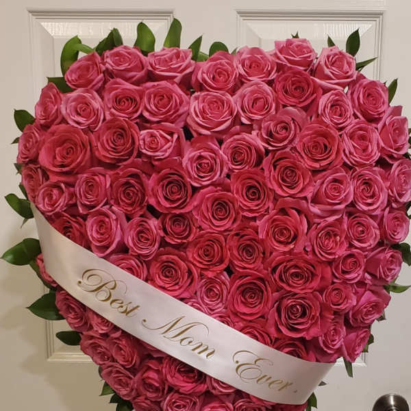 Heart-shaped arrangement of pink roses with a white ribbon