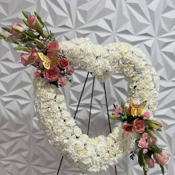 Heart-shaped white floral wreath with pink rose accents on a stand