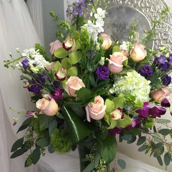 Tall bouquet of pink roses, purple orchids, and white blooms in a glass vase