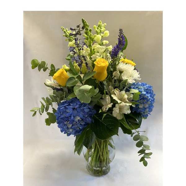 Blue hydrangeas and yellow roses in a clear glass vase