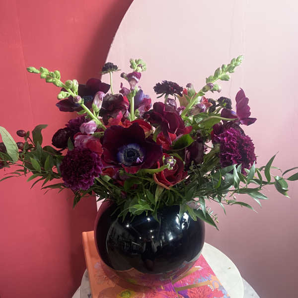 Dark burgundy and purple bouquet in a glossy black vase