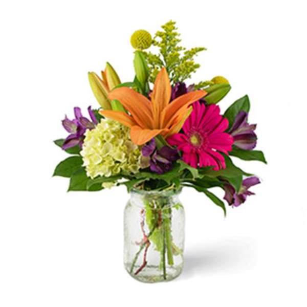 Mixed bouquet with orange lilies, pink gerbera daisies, and purple flowers in a glass vase