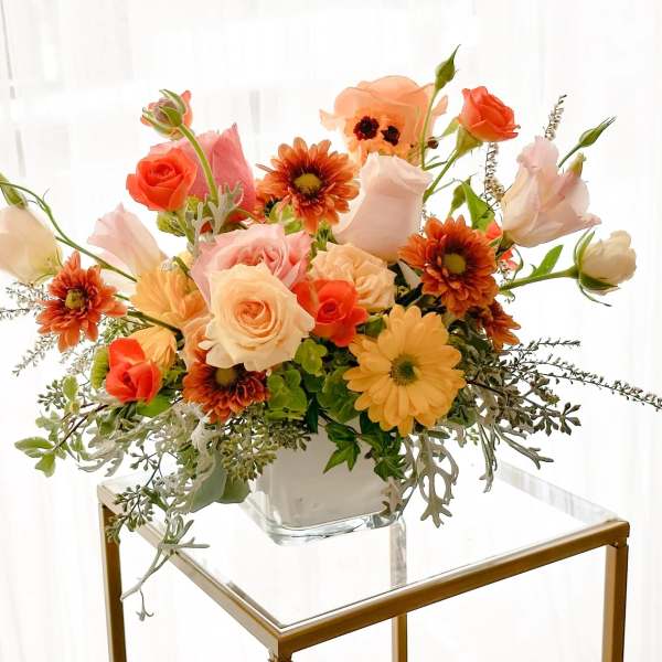 Mixed bouquet of peach, coral, and white flowers in a clear glass vase