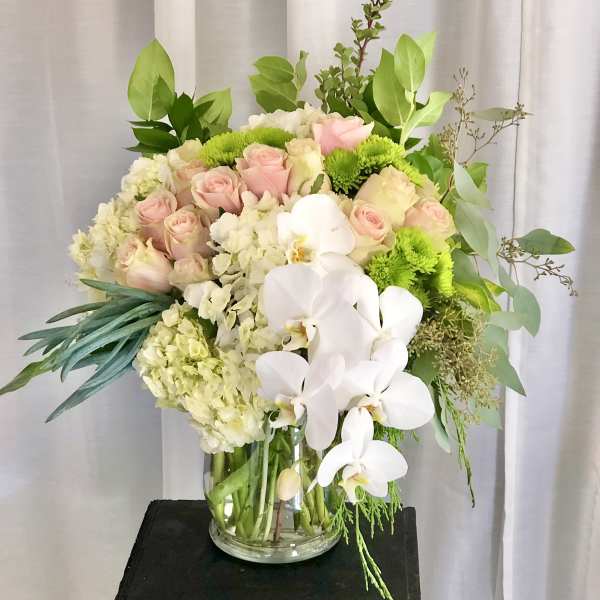 Bouquet of pink roses, white orchids, and green mums in a glass vase