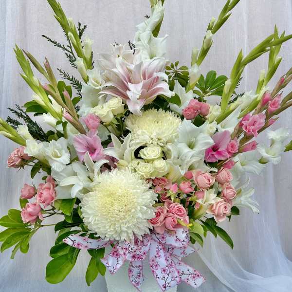 Pink and white floral arrangement in a white vase with a patterned ribbon