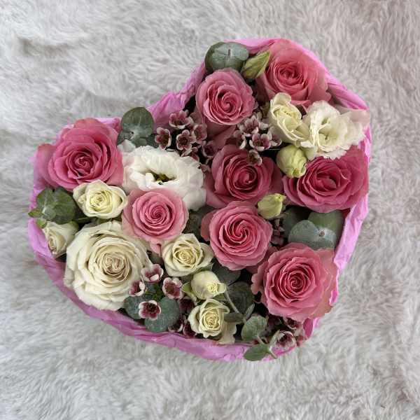 Heart-shaped arrangement of pink and white roses and lisianthus in a pink box