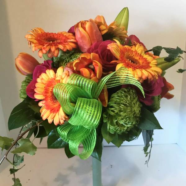 Bouquet of orange and pink flowers in a tall glass vase with a green ribbon
