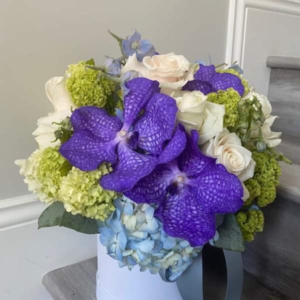 Bouquet of purple orchids, white roses, and blue hydrangeas in a white hat box