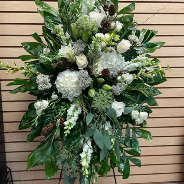 Large white floral standing spray with greenery and pinecones on an easel