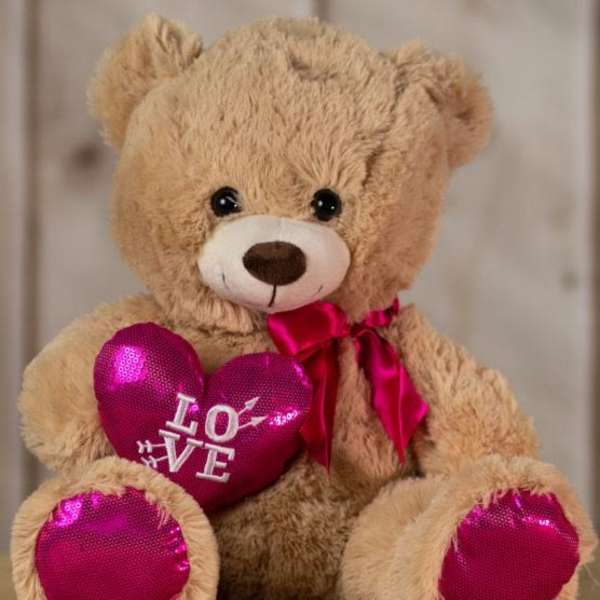 Plush teddy bear holding a pink heart with "LOVE" text