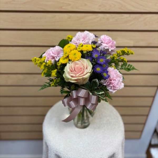 Bouquet of pink, yellow, and purple flowers in a glass vase with a ribbon