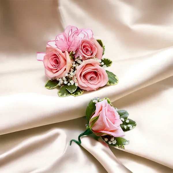 Two pink rose boutonnieres with ribbon accents on satin fabric