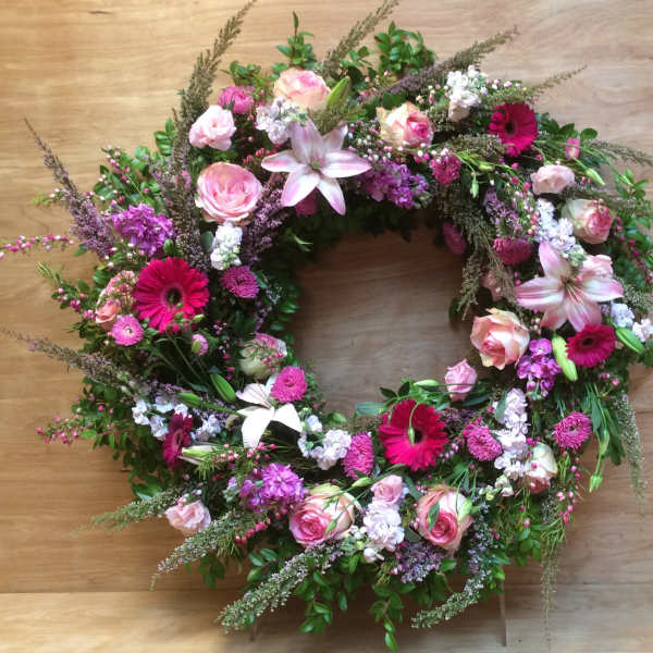 Circular floral wreath with pink roses, lilies, and magenta daisies