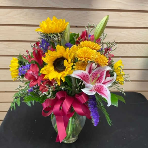 Mixed bouquet with sunflowers, lilies, and a pink ribbon in a glass vase