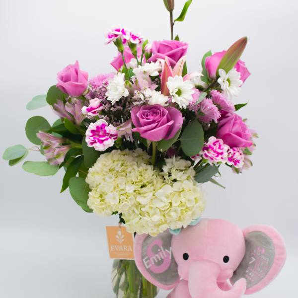 Pink rose bouquet in a glass vase with a plush pink elephant