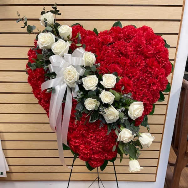 Heart-shaped red carnation wreath with white roses and a white ribbon on an easel