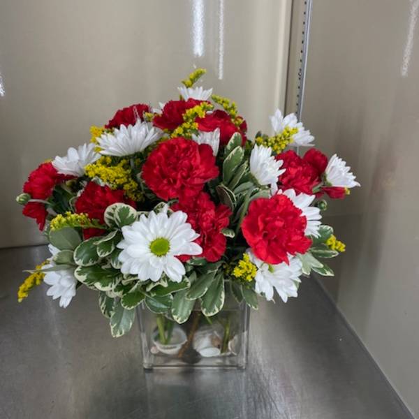 Red carnations and white daisies in a clear square vase