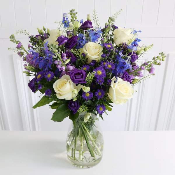 Bouquet of white roses and purple-blue flowers in a clear glass vase