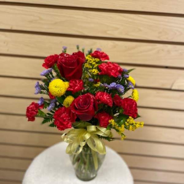 Bouquet of red roses, carnations, and yellow and purple filler flowers in a glass vase