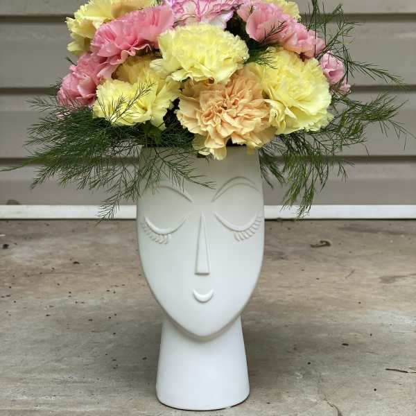 Pastel carnations arranged in a white face-shaped vase
