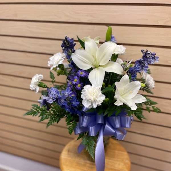 White lilies and blue flowers in a vase with a purple ribbon