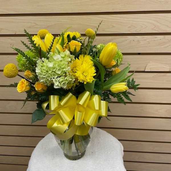 Yellow floral bouquet in a glass vase with a large yellow ribbon